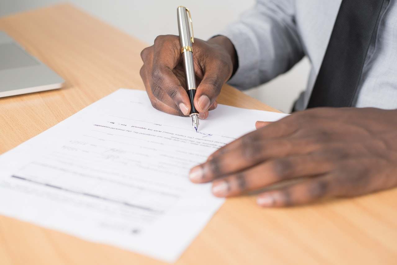 Man wearing navy tie and light grey shirt signing a personal guarantee document.