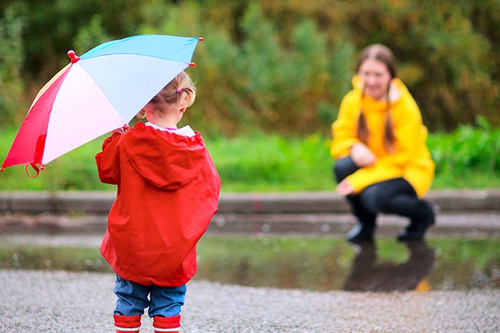 Toddler in red rain jacket and holding an umbrella stands opposite step-mum in yellow rain jacket.