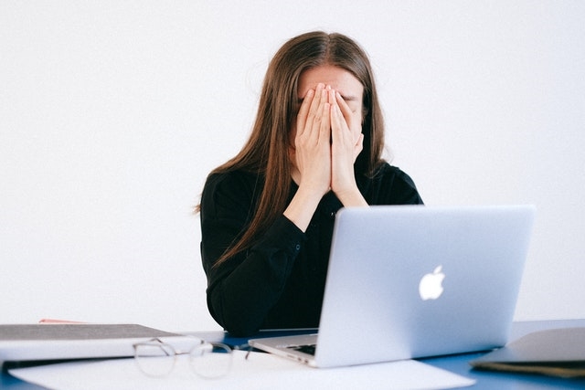 Women in black top sat infront of Macbook laptop with head in hands