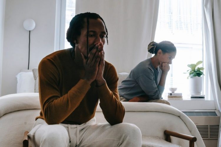 A couple sit on other sides of the bed with their heads in their hands.