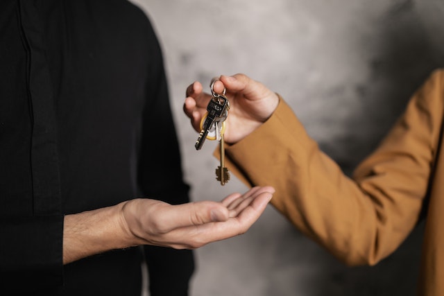 Conveyancer wearing brown jacket and handing new house keys to buyers.