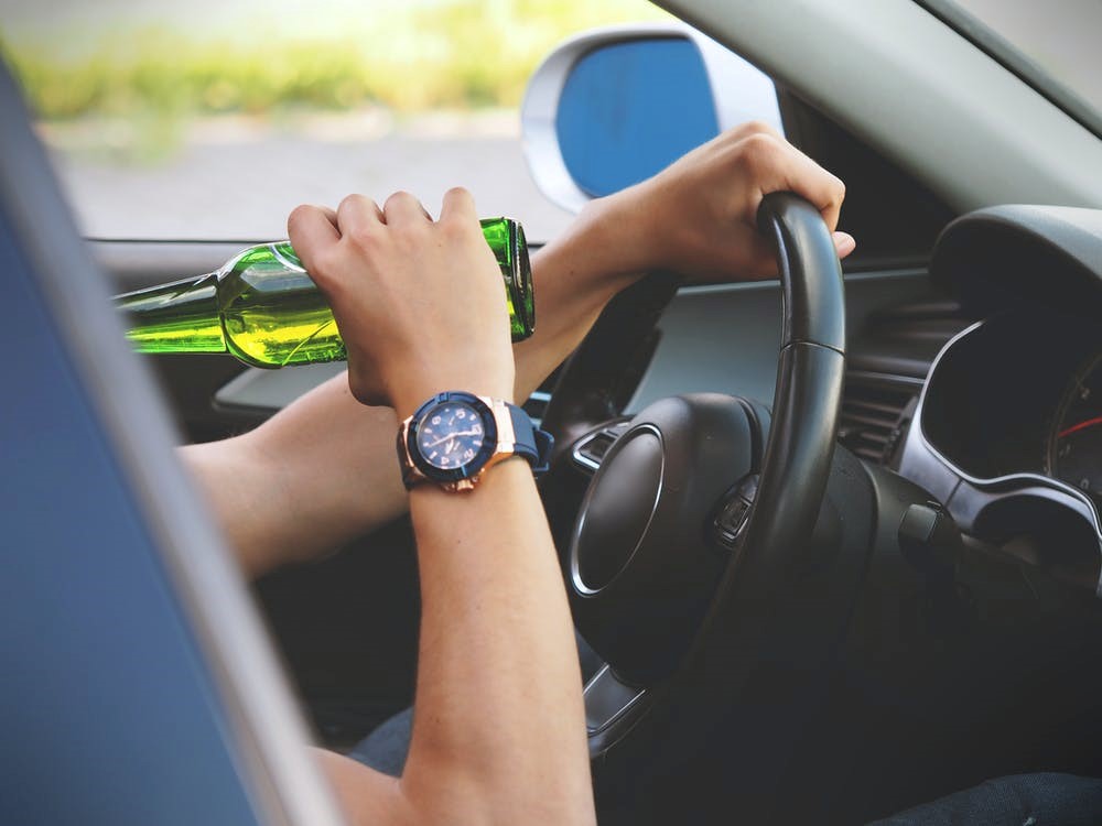 An individual drinking a bottle of beer while driving.