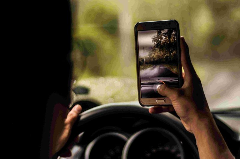 An individual taking a picture on a mobile device while driving.