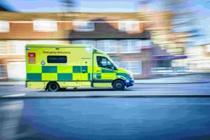 Yellow and green emergency ambulance vehicle racing down a road in the UK.