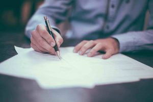 Man wearing blue shirt writing on documents.