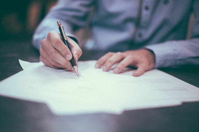 Man wearing light blue shirt sings documents with a black and gold pen.