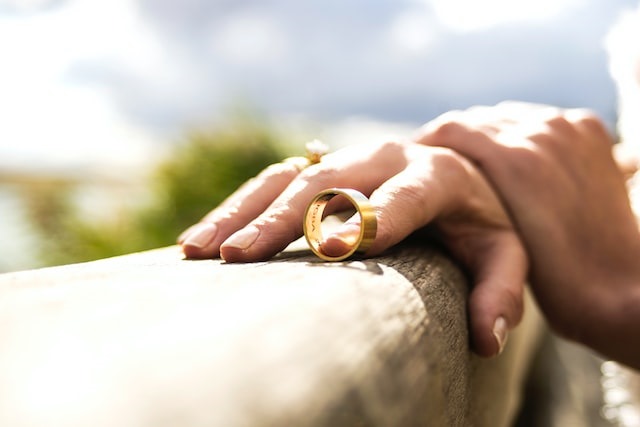 Person's hand rests on the edge of a wall with a gold wedding band removed from their finger and balancing next to their hand.