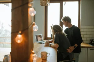 A couple living together, both looking at a laptop.