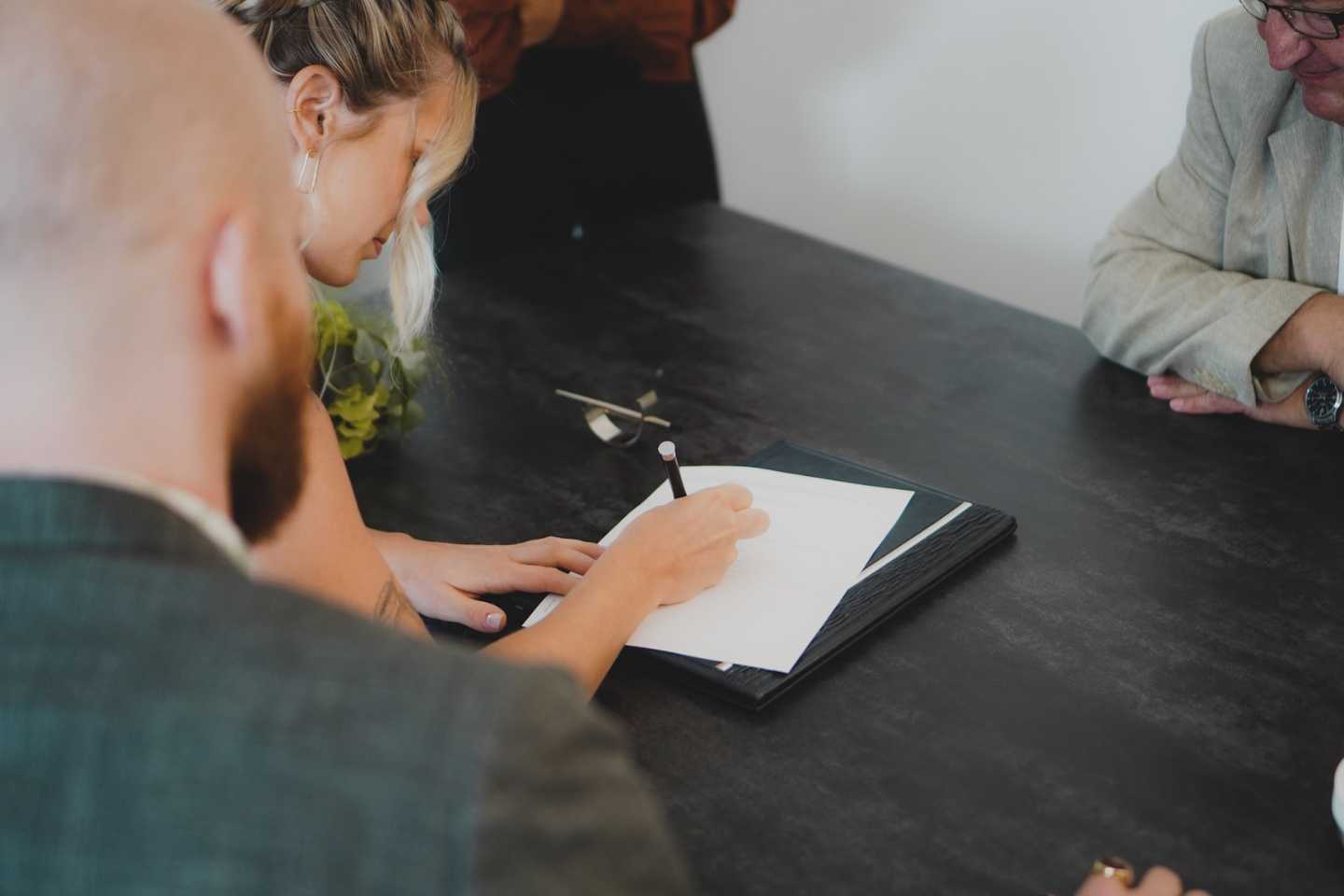 Woman with blonde hair signing a document on a dark desk