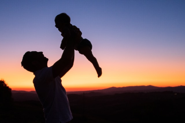 Silhouette of father lifting young child into the air happily during sunset