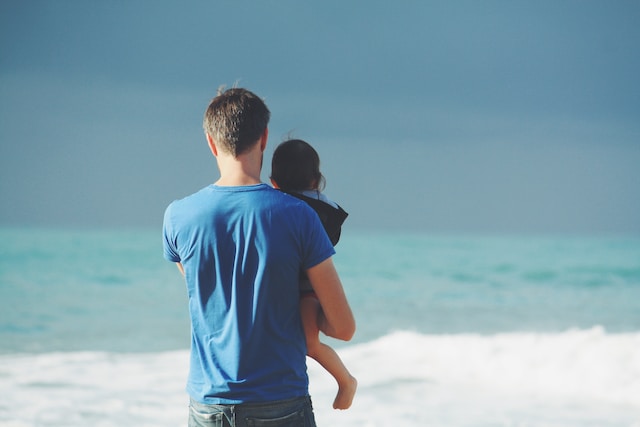 Father holding young daughter and looking out into sea.