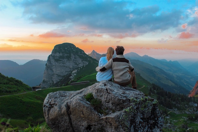 Couple sitting together with their arm around each other looking into the sunset and mountains.