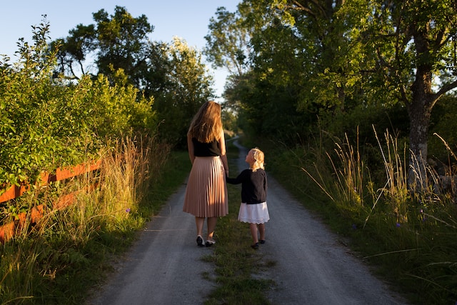 Mother and young daughter holding hands and walking away in the countryside after moving to another place following divorce.