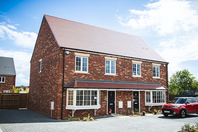 A chain free property for sale. It is a red-brick, new build semi-detached house. A red car is parked in front.