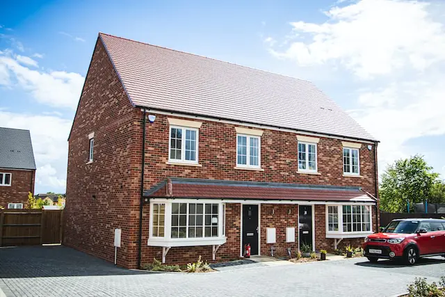 A chain free property for sale. It is a red-brick, new build semi-detached house. A red car is parked in front.