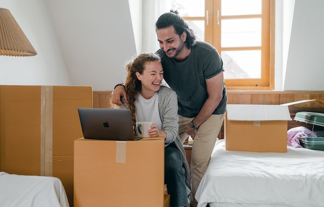 A young couple who are first-time buyers are getting ready to move into their first home. They are smiling whilst packing boxes.