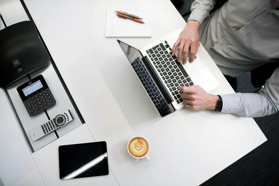 A man sat at a white desk using a laptop.